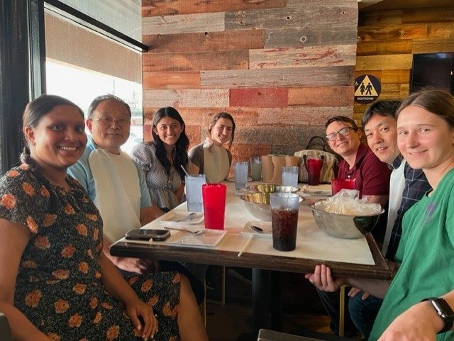 seven students sitting around table smiling while posing at lunch table.
