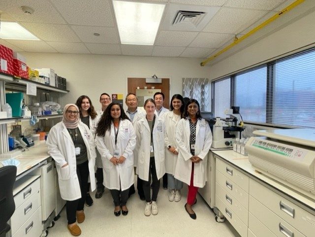 Complete lab staff in white lab coats standing in research lab with Dr. Chandra