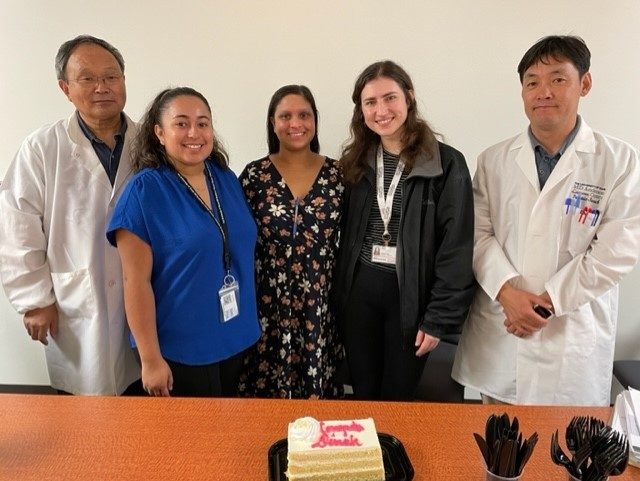 five students posing for picture in front of a farewell cake to student.