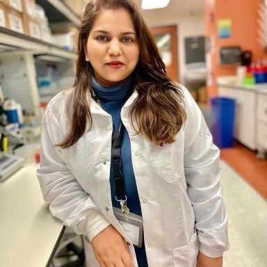 Headshot of a lab member leaning against a bench in the lab, wearing a lab coat