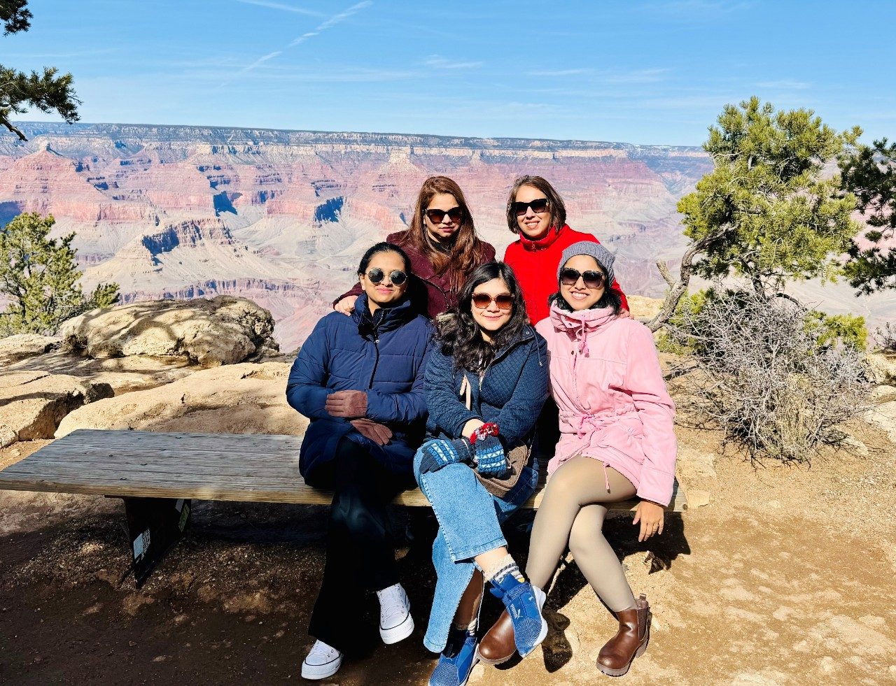 Five lab members in sweaters, jackets, and sunglasses pose outside in a park