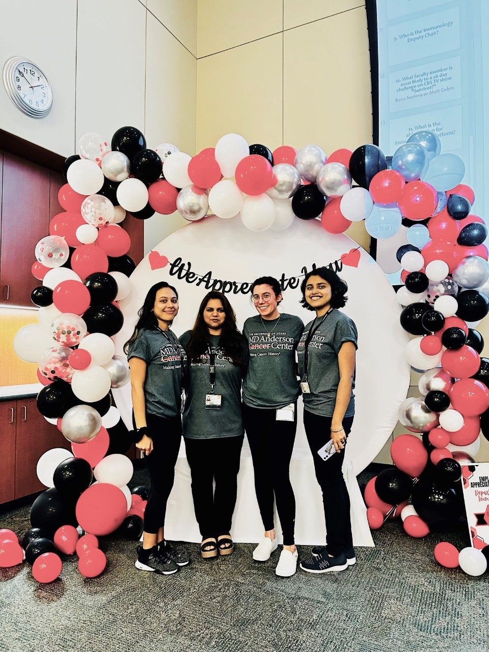 Four lab members posing in a red, black, and white balloon arch, all wearing MD Anderson t-shirts