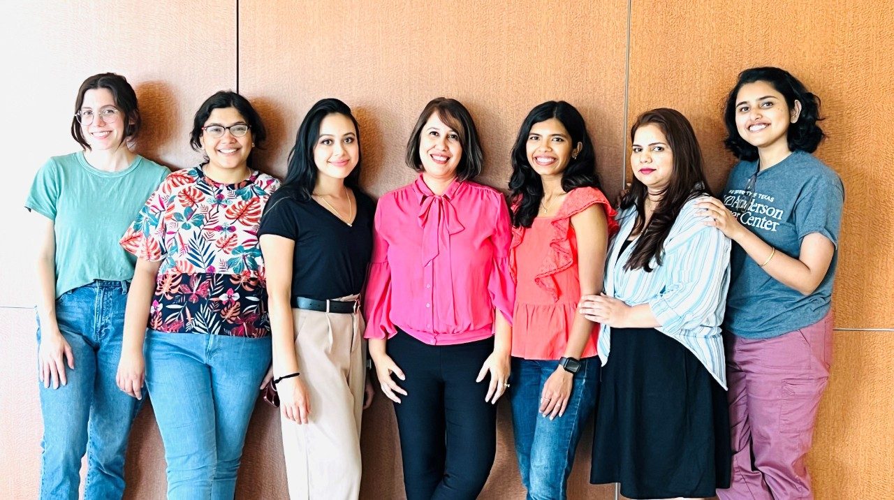 Seven lab members stand in front a wall, posing