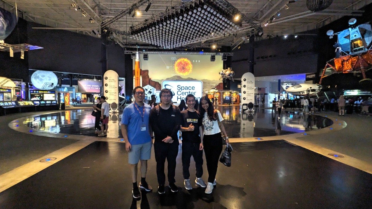 Four people lined up in front of an exhibit at Space Center Houston, smiling at the camera.