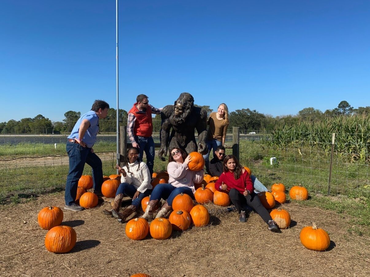 Lab members pose outdoors with a pile of pumpkins and a yeti statue