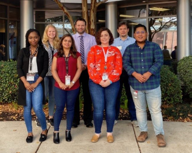 Seven people in two rows, posing for a picture outside of an MD Anderson building