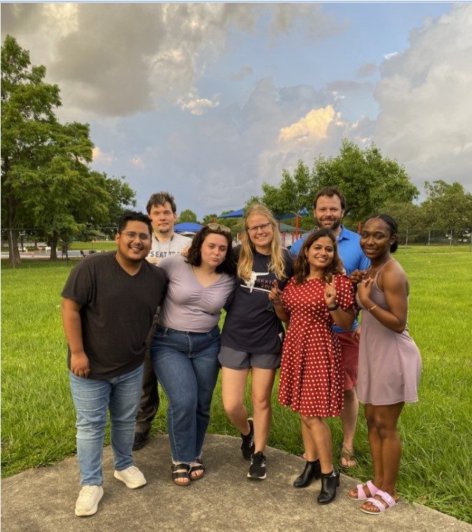 Seven people in a semicircle, posing for a picture outside