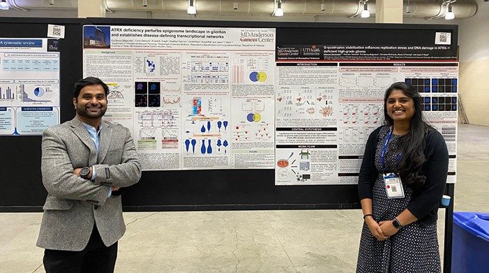 Two lab members stand beside posters