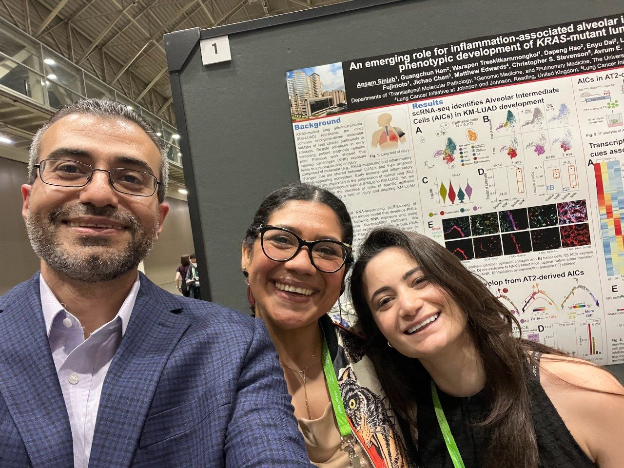 Dr. Kadara and two lab members smiling in a selfie in front of a poster