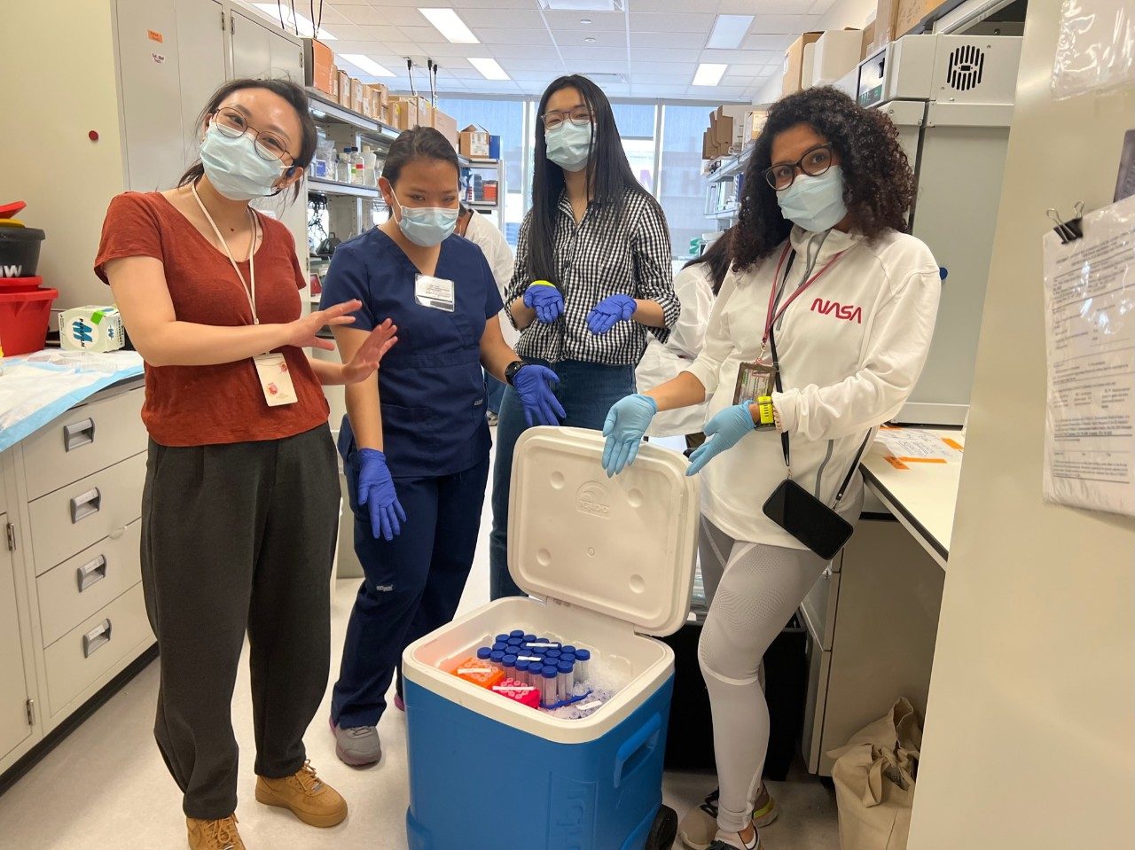 Four people in a lab with masks on pointing into a cooler