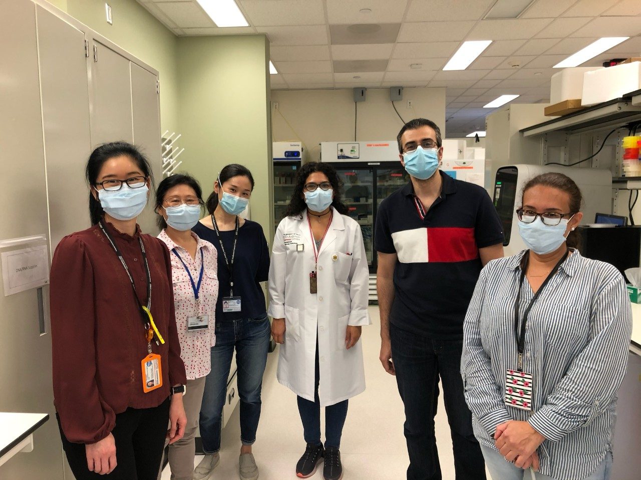 Six people wearing masks lined up for a group photo