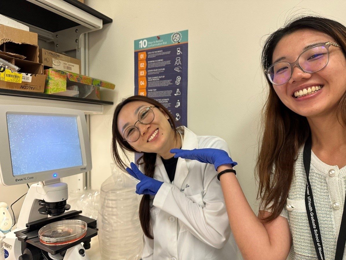 Two lab members with blue lab gloves on pointing at a machine in lab