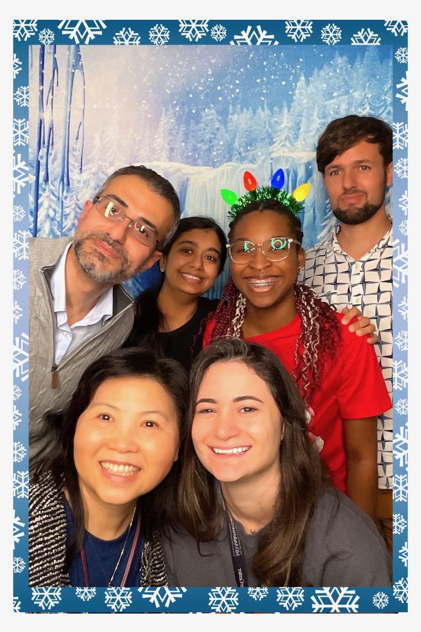 Six lab members in a holiday photo booth with a wintery background