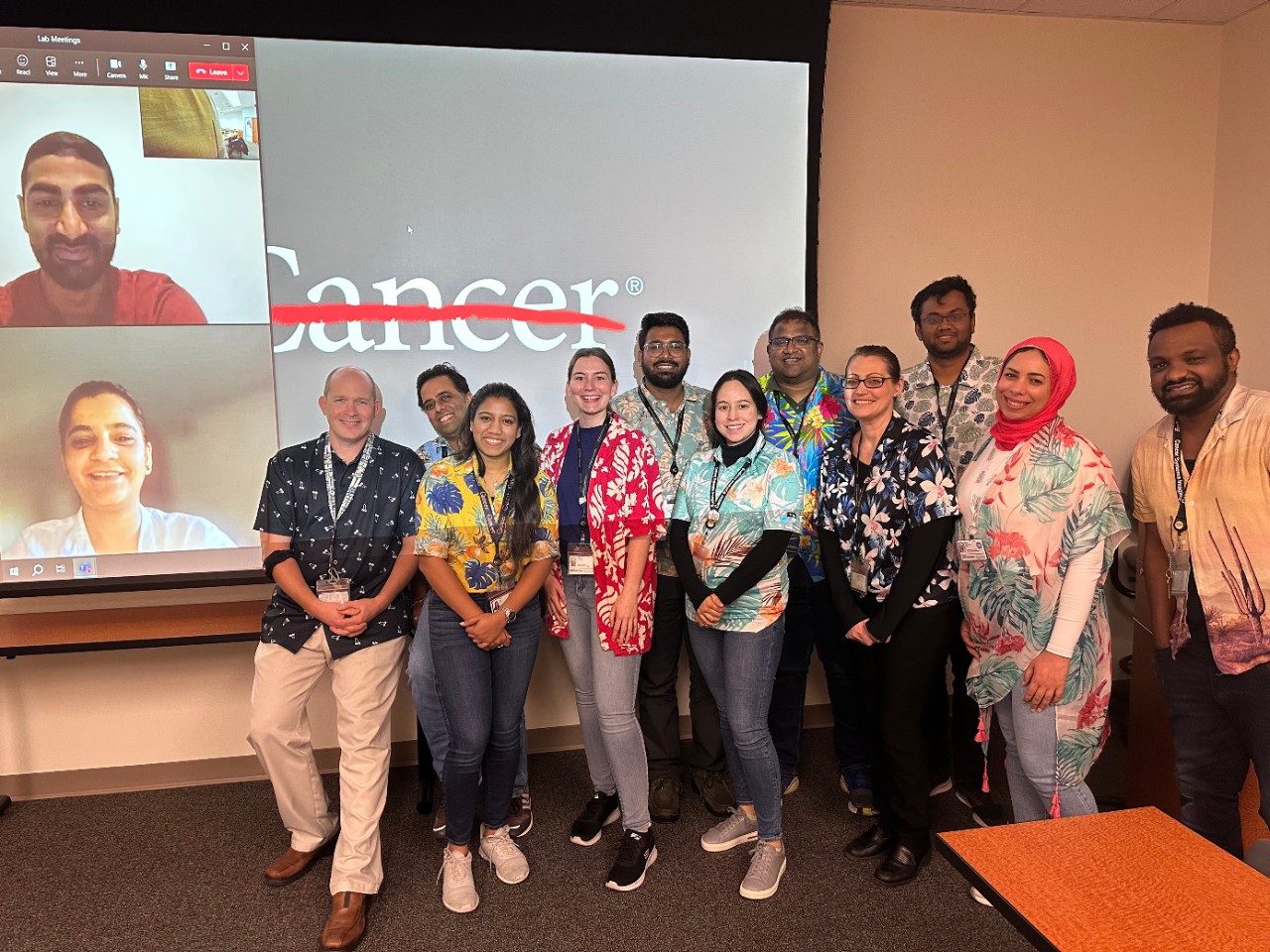 Members of the Quarles Lab pose in Hawaiian shirts at the front of a conference room