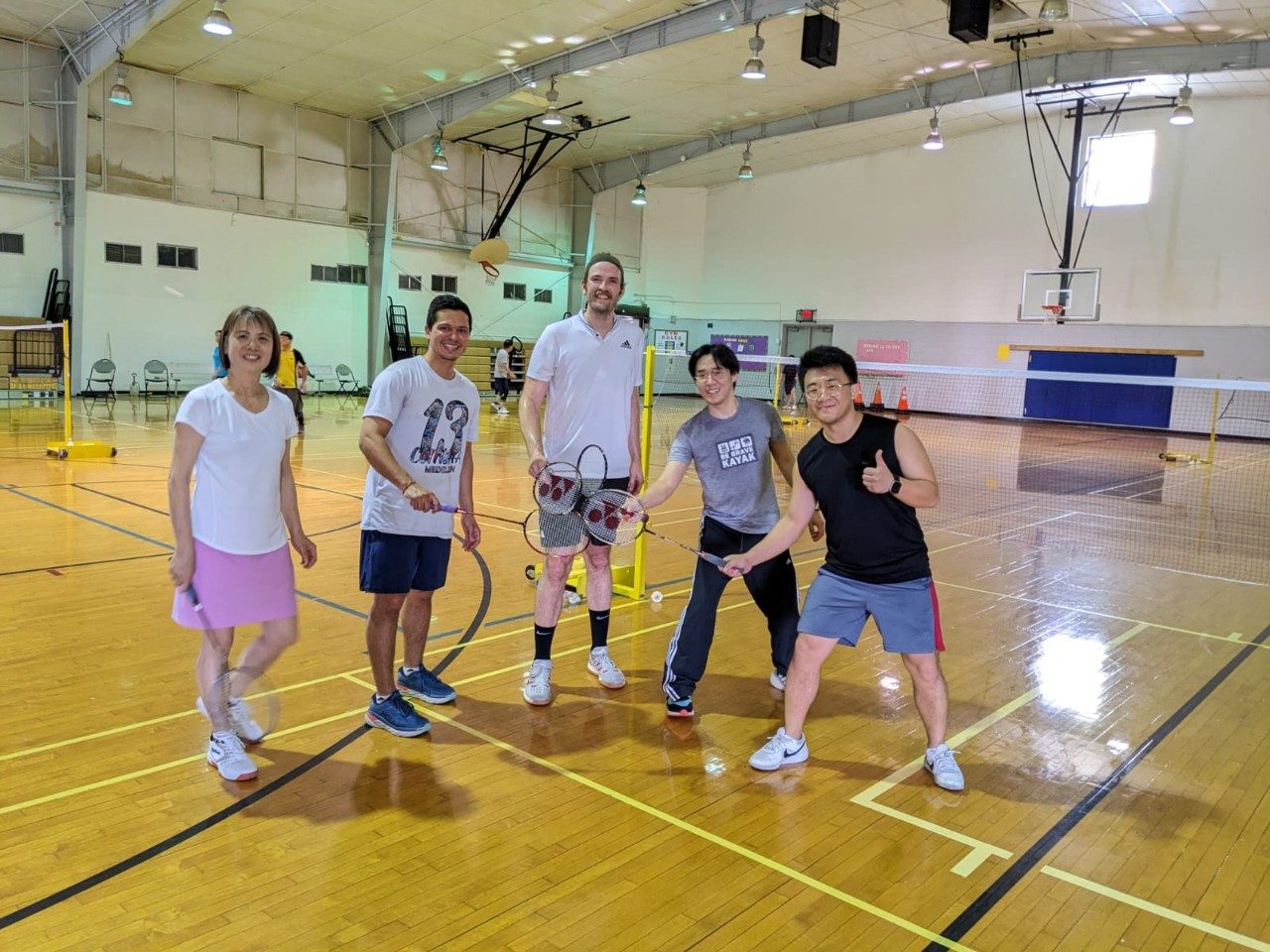 Five people standing on an indoor court holding rackets