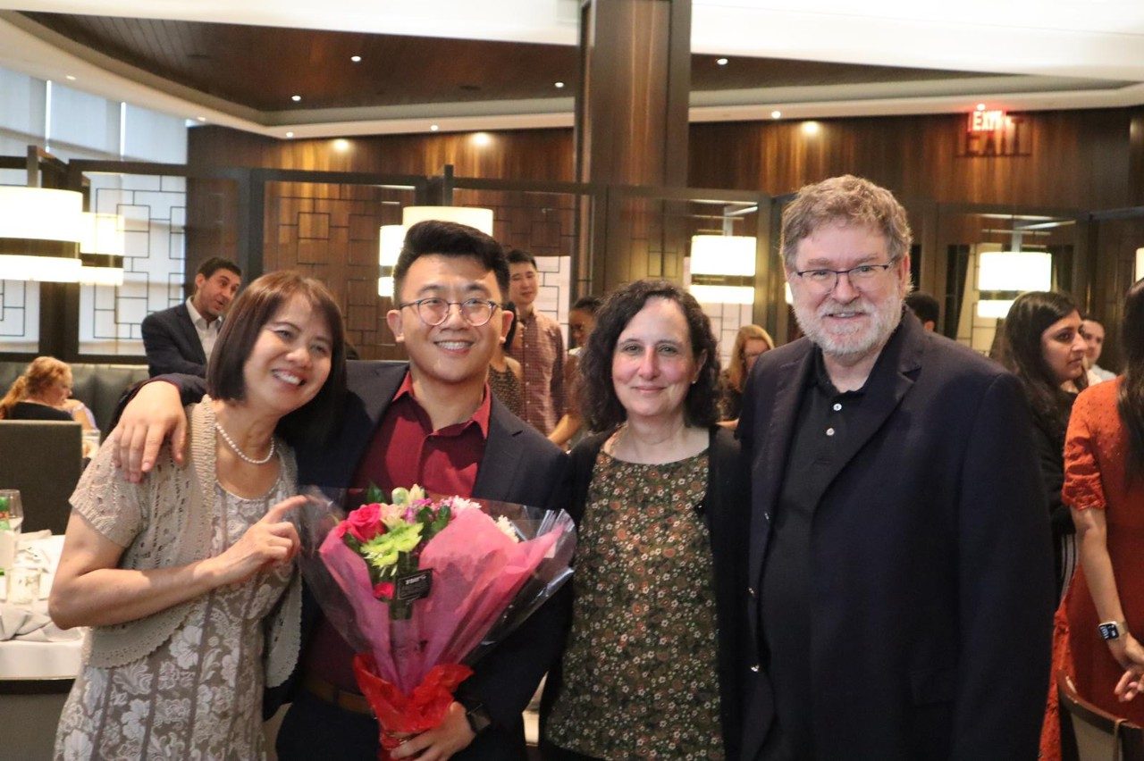 Four people lined up for a photo, with one holding a bouquet of flowers
